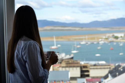 a woman holding a cup in front of a window at Alto Andino Hotel in Ushuaia