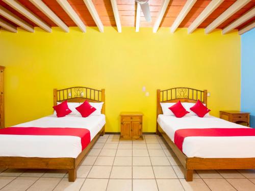 two beds in a yellow room with red pillows at Hotel Posada San Rafael in Oaxaca City