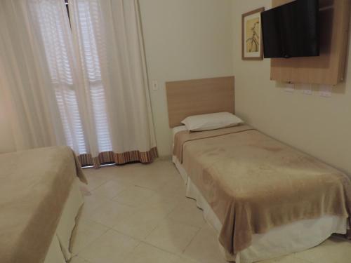 a room with two beds and a tv on the wall at Hotel Costa Balena-Piscina Aquecida Coberta in Guarujá