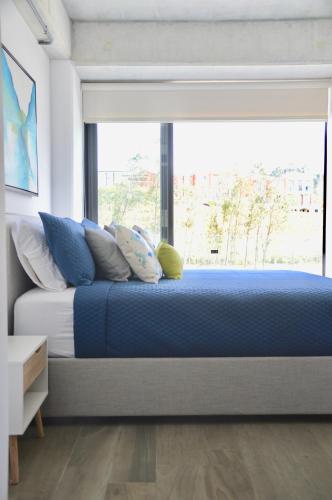 a bedroom with a bed with blue sheets and a window at Cozy Stays Cayala Apartments 4 in Guatemala