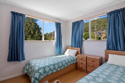 a bedroom with two beds and blue curtains at McFalls Bach - Havelock Holiday Home in Havelock