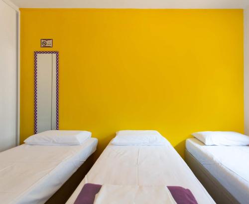 two beds in a room with a yellow wall at MADÁ hostel in Sao Paulo