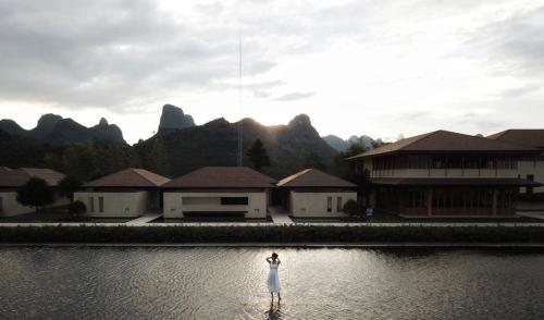 a woman standing in the water in front of some buildings at Misty Wonderland ,Yangshuo Xingping in Yangshuo