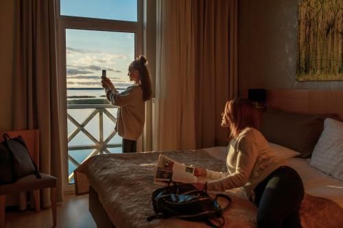 a woman taking a picture of a woman sitting on a bed at Hestia Hotel Haapsalu SPA in Haapsalu