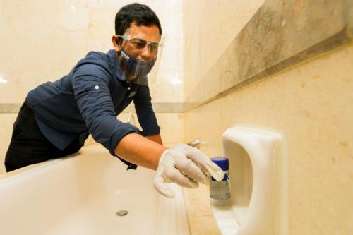 a man in a bathroom cleaning a urinal at Serela Riau by KAGUM Hotels in Bandung