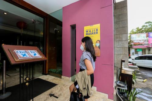 a woman wearing a mask standing outside a pink building at Serela Riau by KAGUM Hotels in Bandung