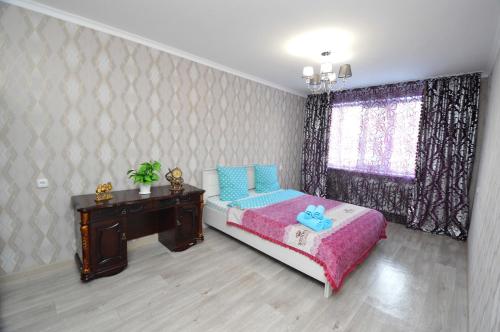 a bedroom with a bed and a desk and a window at Мода в доме 14 in Uralsk