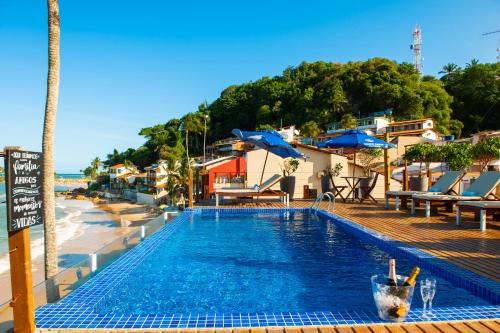 a swimming pool next to a beach with chairs and umbrellas at Pousada Bahia Bacana in Morro de São Paulo