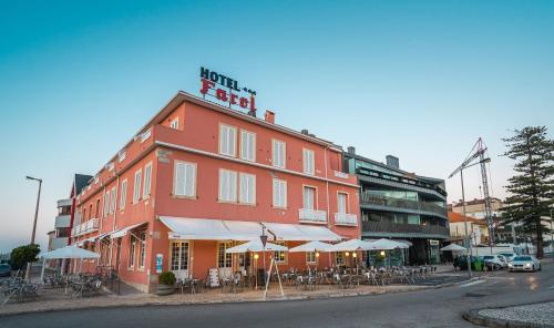 a red building with tables and umbrellas on a street at Hotel Farol in Praia da Barra