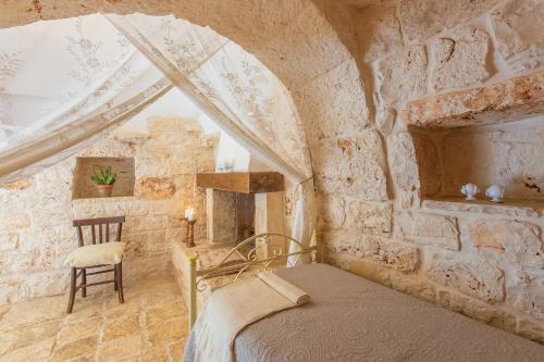 1 dormitorio con 1 cama y 1 silla en una pared de piedra en Trullo con piscina baby, en San Michele Salentino