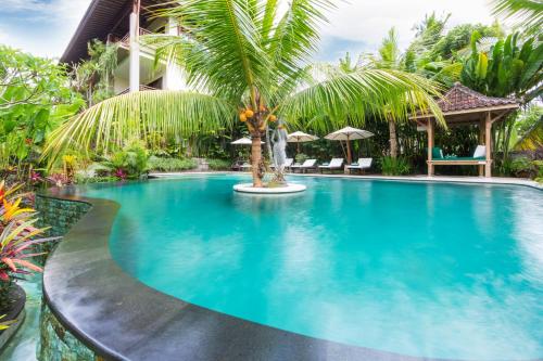 a swimming pool with a palm tree in front of a building at Alamdini Resort Ubud in Ubud