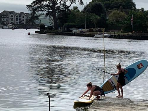 two women are standing on a surfboard in the water at Charming Devon Cottage near Quay-Rain Shower, Restaurants & Free Parking in Kingsbridge
