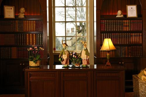 a library with two figurines on a table in front of a window at Washingborough Hall Hotel in Lincoln
