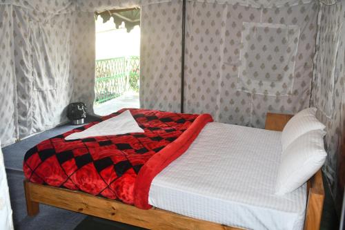 a bed with a red and black blanket and a window at Kodom Bari Retreat, Kaziranga in Kāziranga
