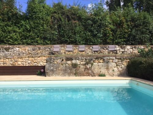 a swimming pool with a bench and a stone wall at Dans la bastide de Domme - piscine chauffée, parking privé in Domme