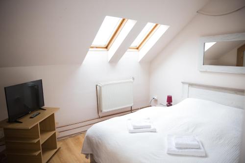 a white bedroom with a bed and a tv at Apartament Delta in Bistriţa