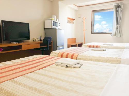 a hotel room with two beds and a desk with a television at Hotel Peace Island Miyakojima in Miyako Island