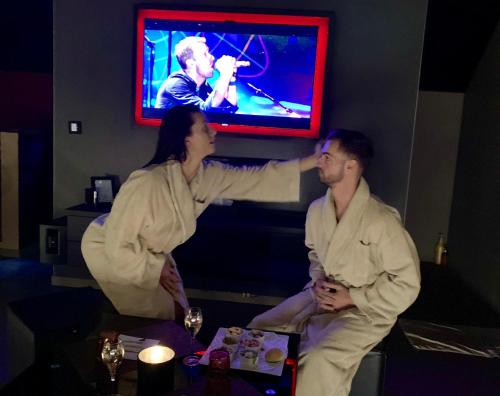 a man and a woman sitting in front of a tv at Octavie - Suite de luxe à Tournai avec piscine privée, jacuzzi, sauna et hammam in Tournai