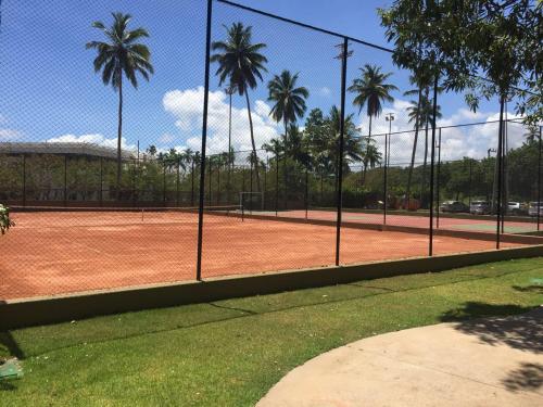 a tennis court with palm trees behind a fence at FLAT MARULHOS in Ipojuca