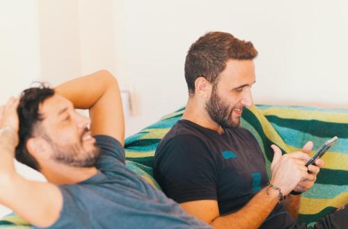 two men sitting on a couch looking at a cell phone at SIGRUM Hostel in San Rafael