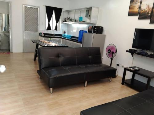 a living room with a black couch and a kitchen at 2BR townhouses good for 12pax each & NETFLIX & 100Mbps WIFI & pool resort 2min walk & 3km outside Pico de Loro Cove & Calayo Cove - with Endorsement for Pico de Loro Cove good for 7 days & Boat-Tour & Island Hopping assistance in Nasugbu