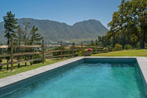 a swimming pool with a fence and mountains in the background at High Season Farm Luxury Cottages in Hermanus