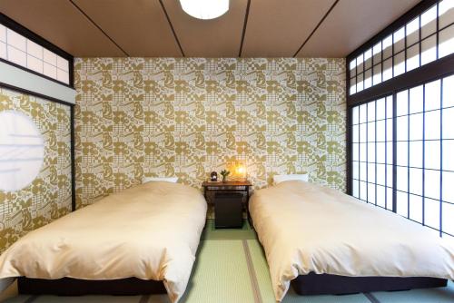 two beds in a room with wallpaper and windows at Ikaho Syusuien in Shibukawa