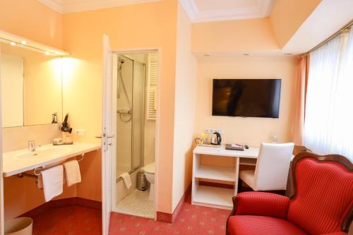 uma casa de banho com uma cadeira vermelha, uma secretária e um lavatório. em Hotel Modena em Bad Steben
