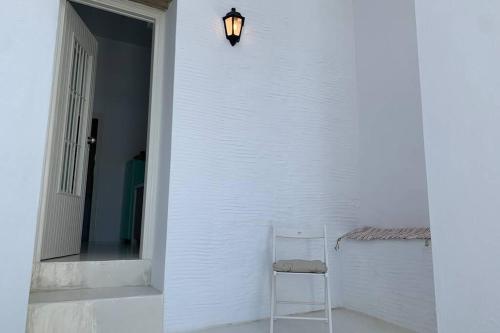 a white chair sitting next to a white wall with a light at Ευημερία in Andros