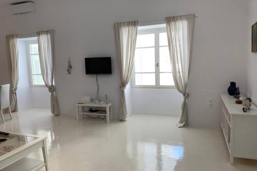 a white living room with a tv and windows at Ευημερία in Andros