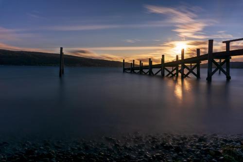 a pier on a lake with the sun setting at Strandhotel Löchnerhaus in Reichenau