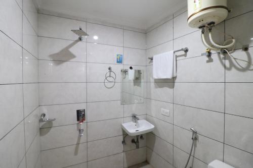 W wyłożonej białymi kafelkami łazience znajduje się umywalka i prysznic. w obiekcie Hotel Airport Paradise w Nowym Delhi