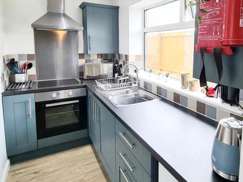 eine Küche mit blauen Schränken, einem Waschbecken und einem Fenster in der Unterkunft Ladybird Cottage, Dog Friendly, Couples or Small families, Yorkshire Wolds - Countryside and Coast in Great Driffield