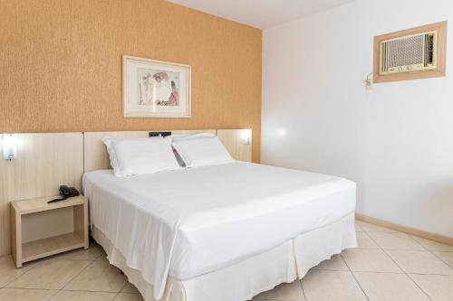 a bedroom with a large white bed and a table at Hotel Açores in Balneário Camboriú
