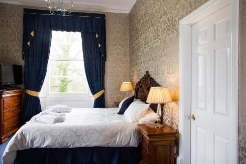 a bedroom with a bed with blue curtains and a window at Elm Grove Country House in Tenby