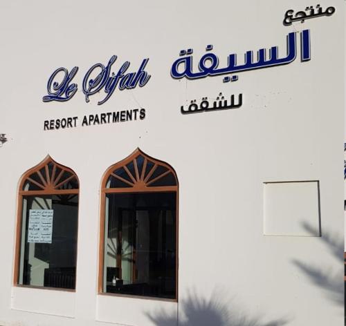znak na boku budynku z dwoma oknami w obiekcie Le Sifah - Marina View Apartments & Villa w mieście As Sifah