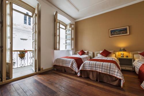 two beds in a room with two windows at Hotel La Orquidea in Cuenca