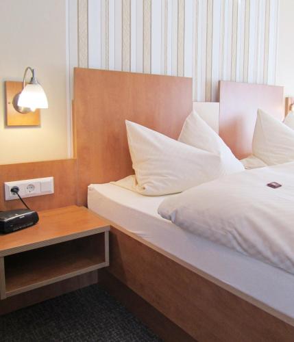 a bed with white sheets and pillows next to a table at Pension Haus Waldfrieden, MeineCardPlus inklusive in Willingen
