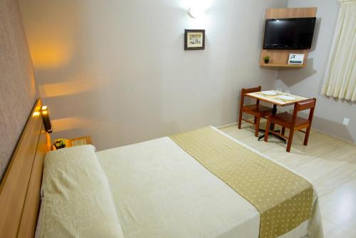 a hotel room with a bed and a table and a television at Hotel Iporã in Itapetininga