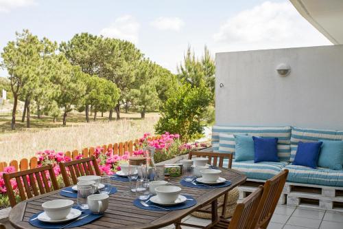 a wooden table with chairs and a couch on a patio at Casa de Férias - Troia Terrace Lake & Pool - Soltroia Comporta Aluguer in Troia
