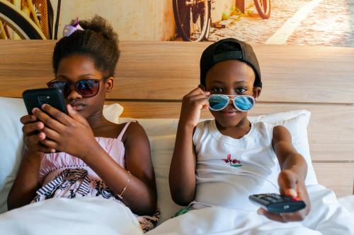 two girls sitting on a bed looking at their cell phones at Novotel Curitiba Batel in Curitiba