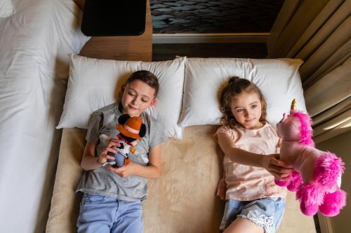 a boy and a girl laying on a bed with stuffed animals at Novotel Curitiba Batel in Curitiba
