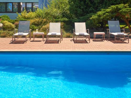 a group of three lounge chairs and a swimming pool at Novotel Poznań Malta in Poznań