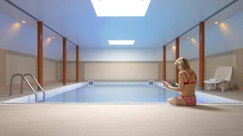 a woman sitting next to a swimming pool at Crowne Plaza Hotel Brugge by IHG in Bruges
