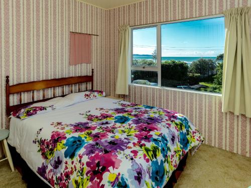 a bedroom with a bed with a floral bedspread and a window at Karoola - Waimarama Bach in Waimarama
