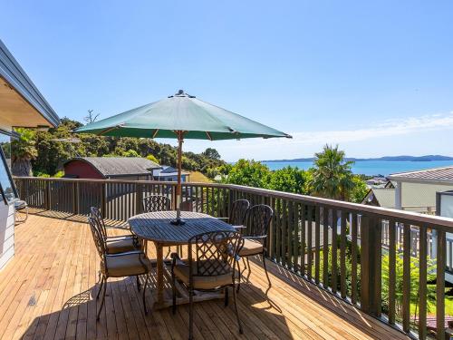 a table and chairs on a deck with an umbrella at Kawau Vista - Snells Beach Holiday Home in Snells Beach