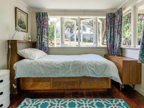 a bedroom with a bed and a window at Onetangi Beach Cottage - Onetangi Bach in Onetangi