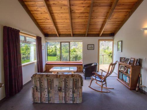 a living room with a table and a chair and windows at Tasman Hideaway - Marahau Holiday Home in Marahau