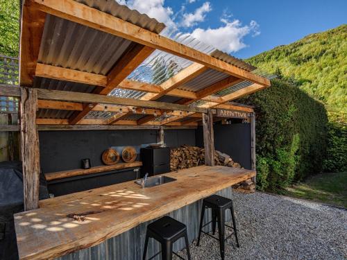 an outdoor kitchen with a wooden table and stools at The Hillvue with Spa - Arrowtown Holiday Home in Arrowtown