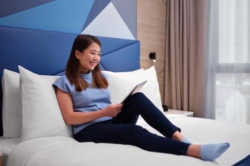 a woman sitting on a bed reading a book at Holiday Inn Express Singapore Serangoon by IHG in Singapore